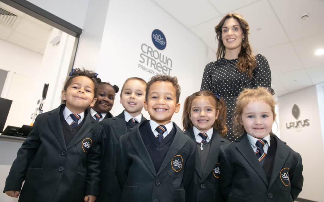 Head of Crown Street Primary School and pupils stand smiling in front of the school reception